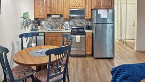 A compact kitchen with wooden cabinets, a stainless steel refrigerator, a microwave, and a stove. There is a dining table with chairs and a blue blanket on the floor. - The Grand Duplex of Silvercreek Inn. Combination of two lock off units. (Granby)