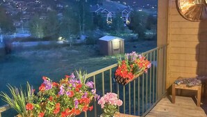 A wooden deck with a table and chairs, potted plants with flowers, and a view of a town at sunset. - The Grand Duplex of Silvercreek Inn. Combination of two lock off units. (Granby)