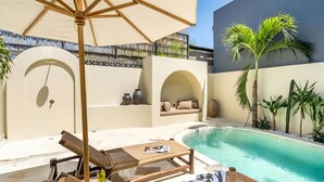 Un área junto a la piscina con sillones reclinables, una sombrilla grande y un rincón de estar con cojines.