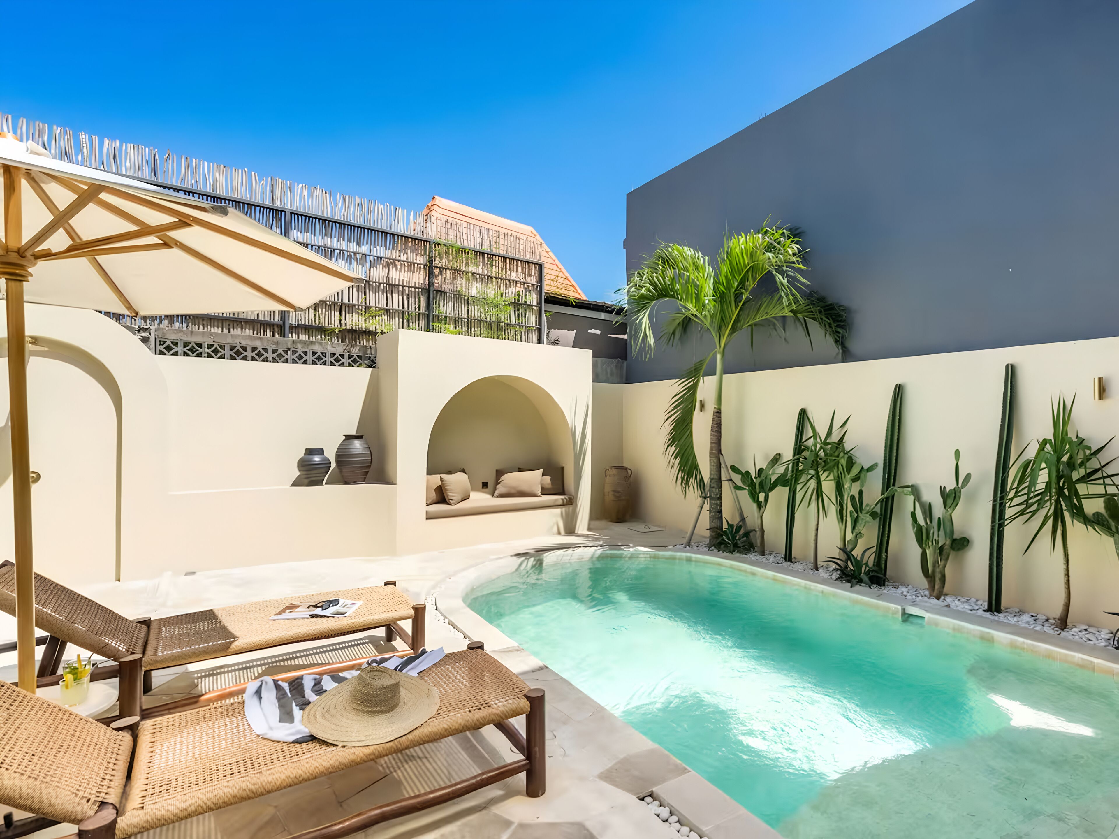 Ein Poolbereich mit Liegestühlen, Sonnenschirm und einer kleinen Sitzecke mit Kissen.