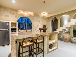 A modern kitchen with a stone backsplash, stainless steel refrigerator, and two bar stools. - Kaktus Villa Pererenan | Luxury 1BR Private Pool Villa (Badung Regency)