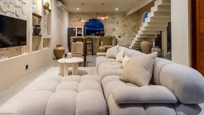 Un interior moderno con un sofá modular, una mesa redonda y una cocina con pared de piedra y arco azul.