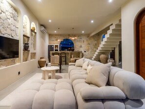 A modern interior with a sectional sofa, a round table, and a kitchen area with a stone wall and blue arch. - Kaktus Villa Pererenan | Luxury 1BR Private Pool Villa (Badung Regency)
