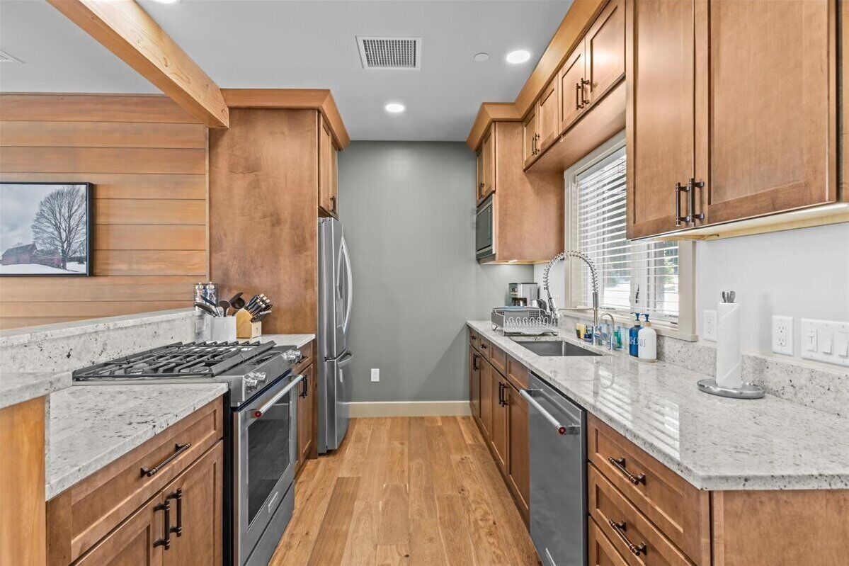 A modern kitchen with wooden cabinets, a stainless steel refrigerator, a built-in oven, and a granite countertop.