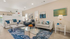 A modern living room with a glass coffee table, two sofas, a white side table, and a decorative wall piece.