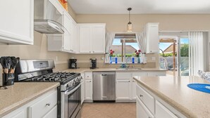 A modern kitchen with white cabinets, stainless steel appliances, and a view to the outside.