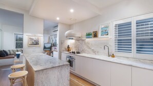 Una cocina moderna con una isla de mármol, armarios blancos y un amplio ventanal con persianas.
