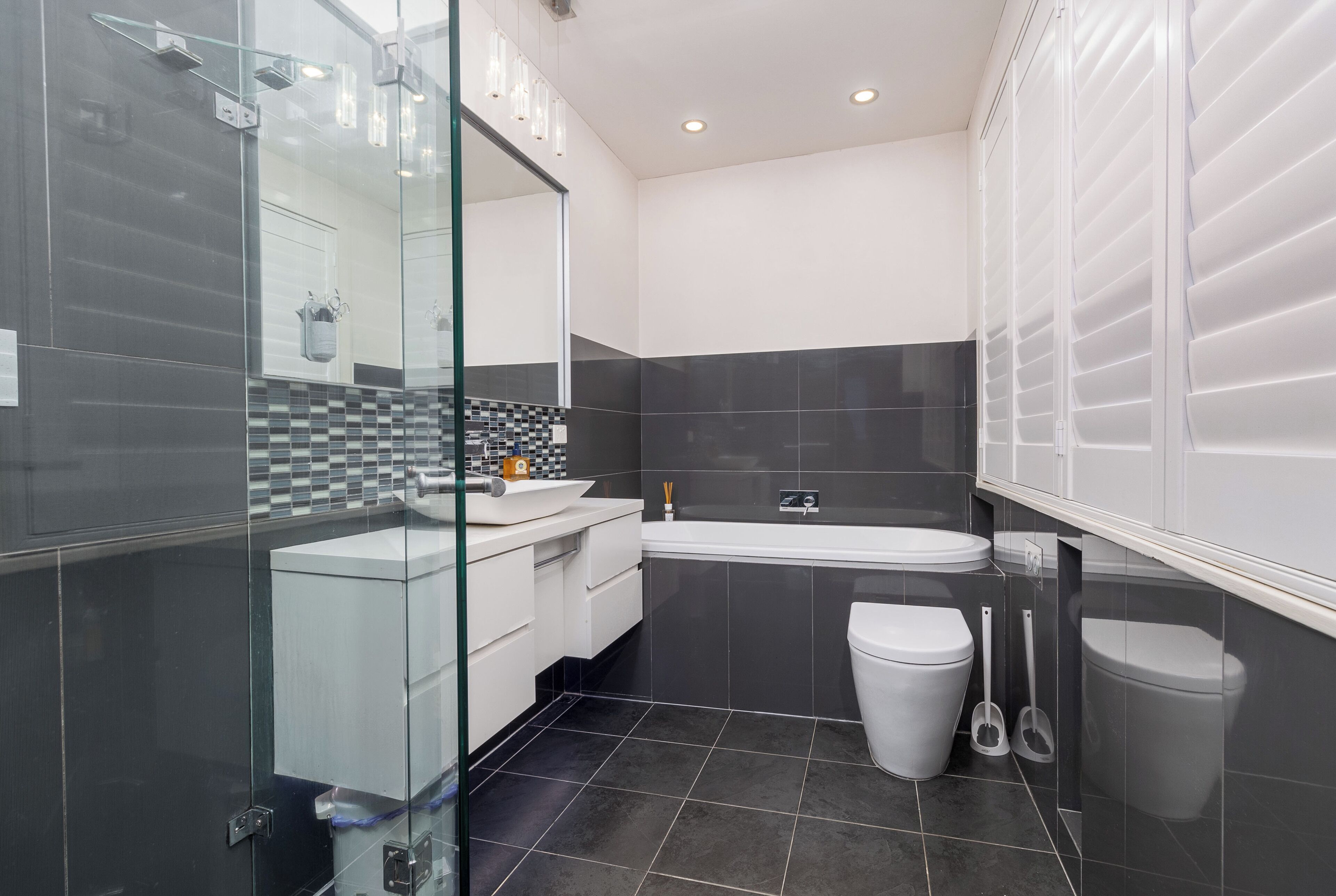 A modern bathroom with a glass shower enclosure, a white sink, a bathtub, and two toilets.