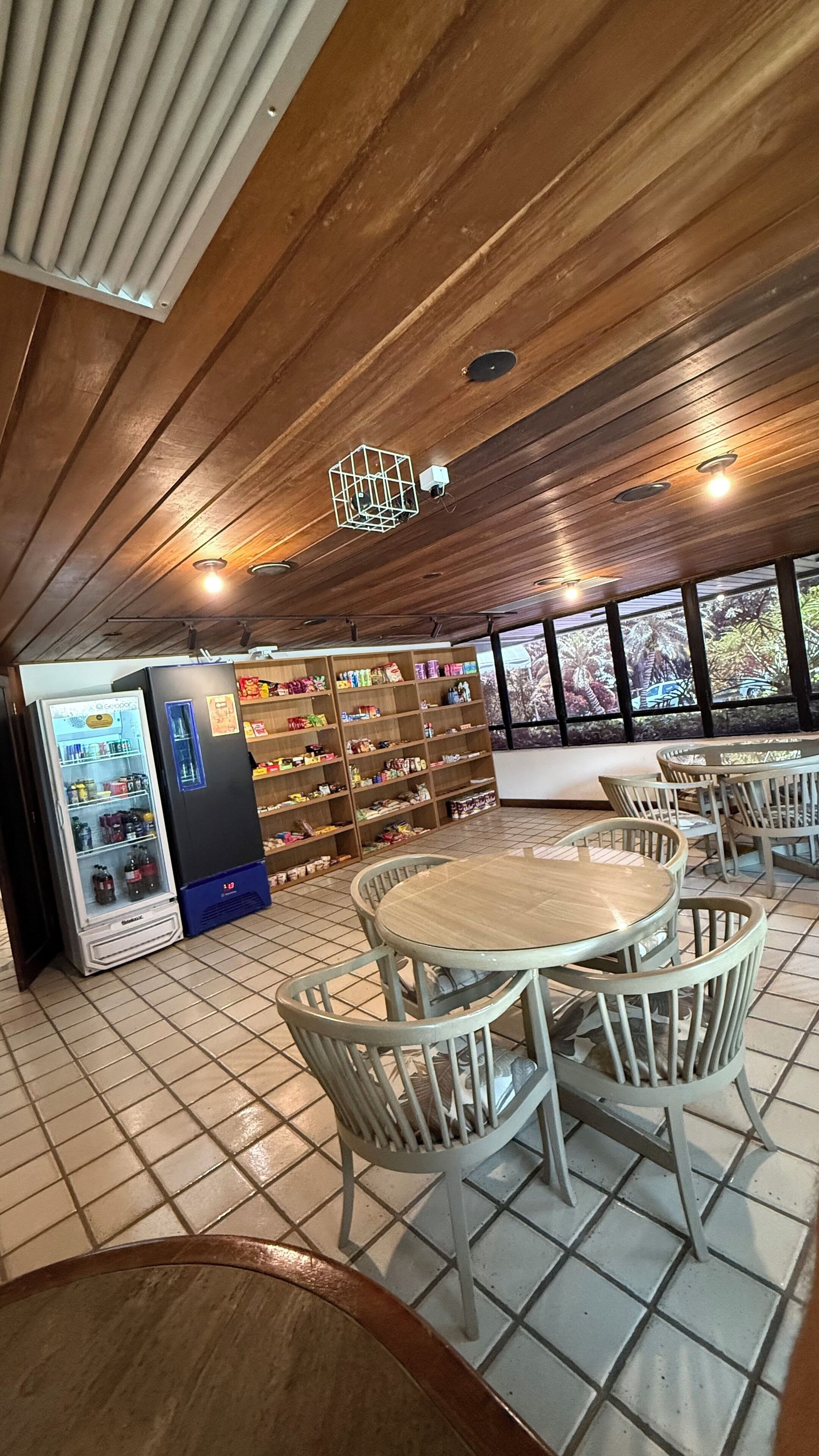 A restaurant with a wooden ceiling, round tables, and chairs. There is a vending machine and shelves with snacks.
