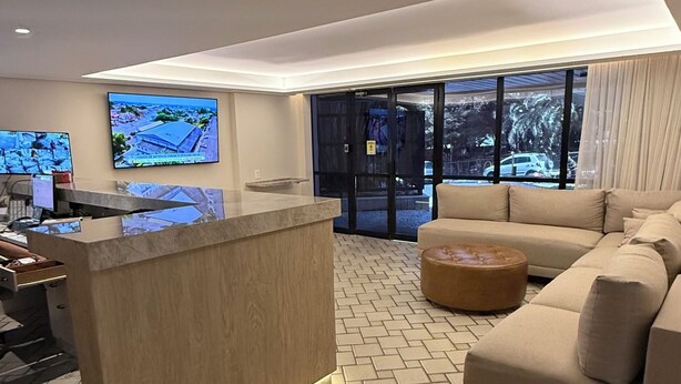 A modern living room with a sofa, a coffee table, and a reception desk. - Apart Hotel recém reformado TV de cinema (Salvador)