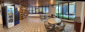 A cafe with a tiled floor, a vending machine, shelves with snacks, and a view through large windows. - Apart Hotel recém reformado TV de cinema (Salvador)