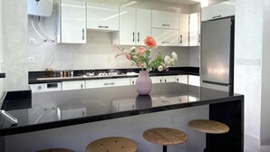 A modern kitchen with white cabinets, a black countertop, a stainless steel refrigerator, and a vase with flowers on the island.