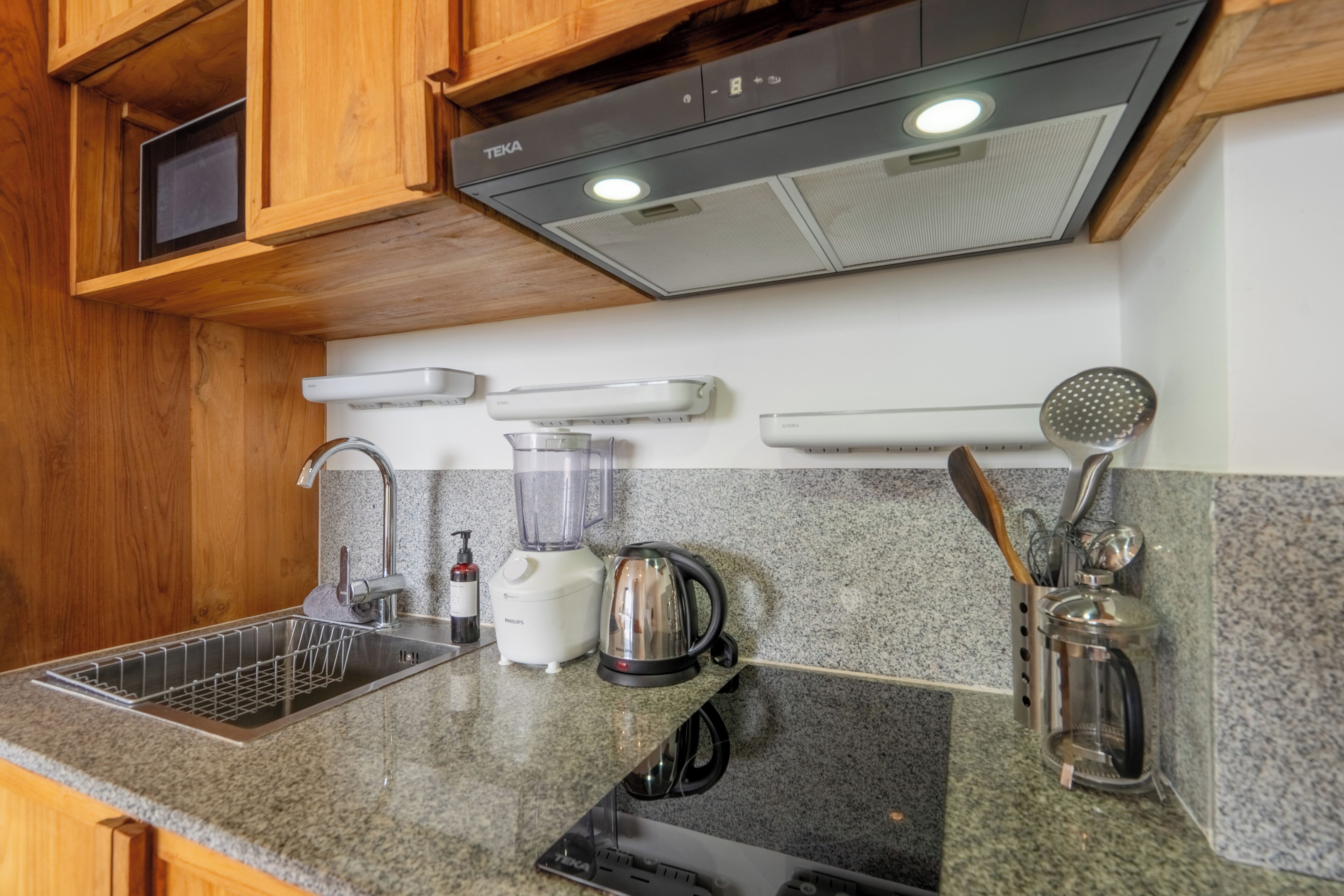 Una cucina con forno a microonde integrato, bollitore, frullatore e macchina del caffè sul piano di lavoro.
