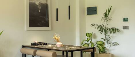 A dining area with a table set for four, a large framed artwork above, pendant lights, and potted plants.