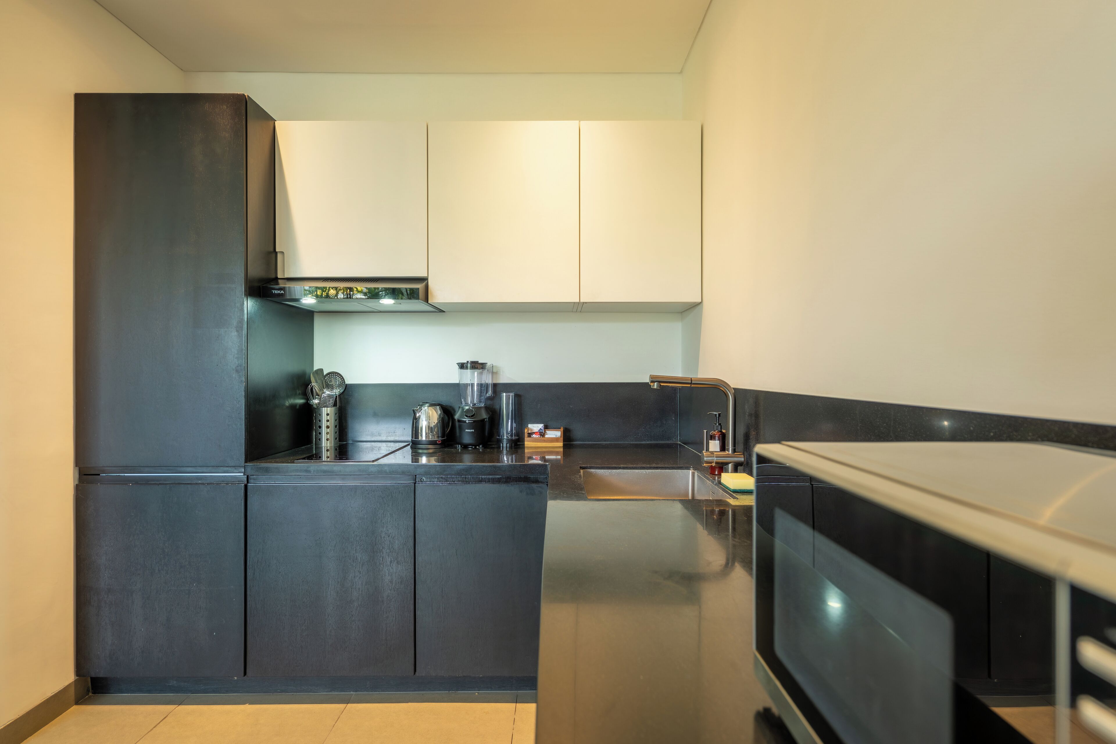 A modern kitchen with dark cabinetry, a stainless steel range hood, a built-in oven, and a microwave.