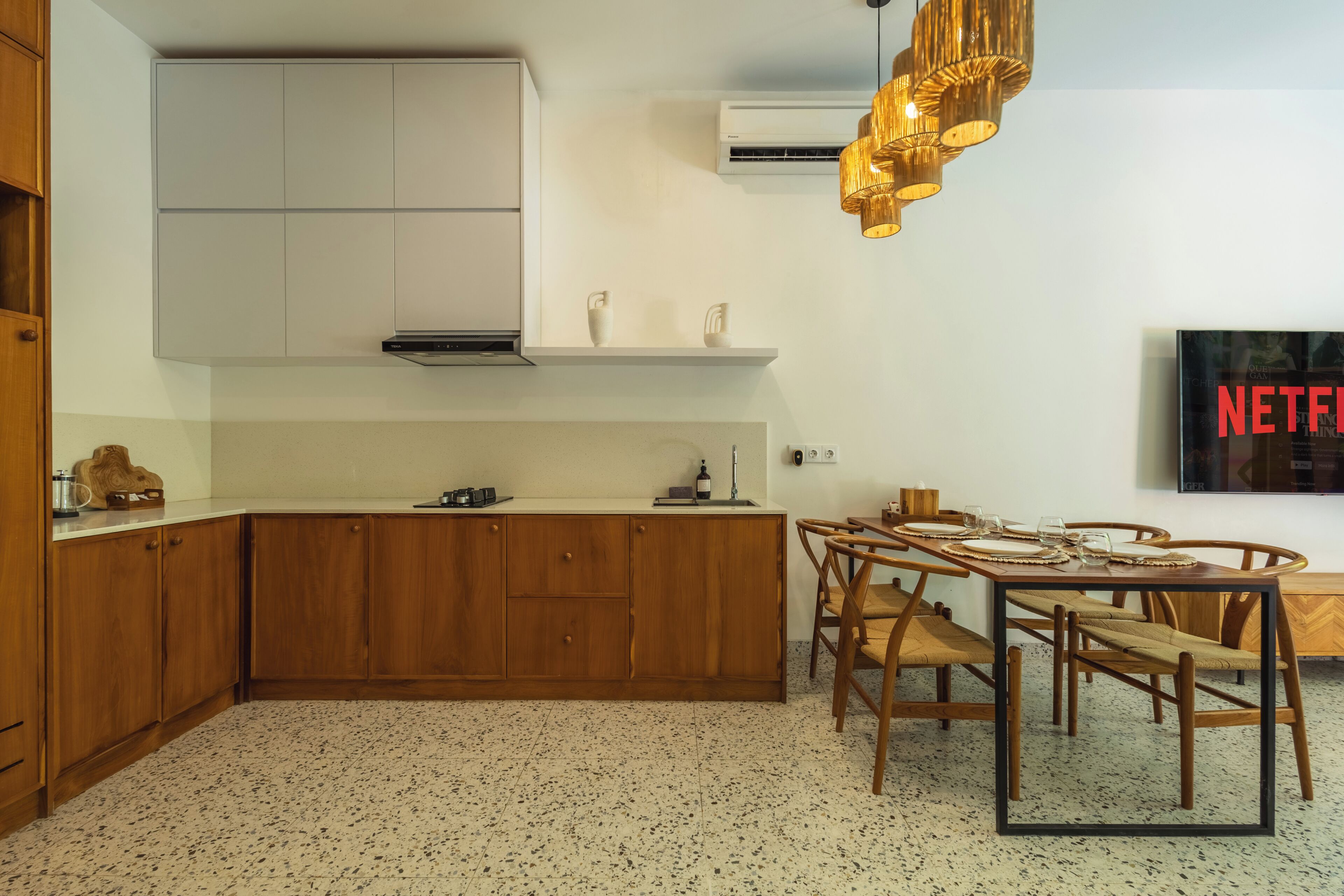 A modern kitchen with wooden cabinets, a dining table with chairs, and a mounted television.