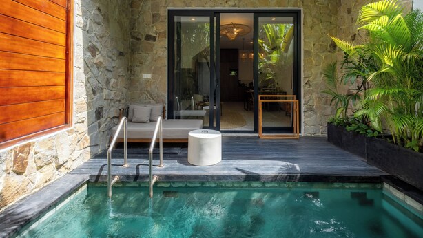 A swimming pool with a glass enclosure, a wooden deck, and a stone wall. - Sunny Aparts 1 by Betterplace (Tibubeneng)