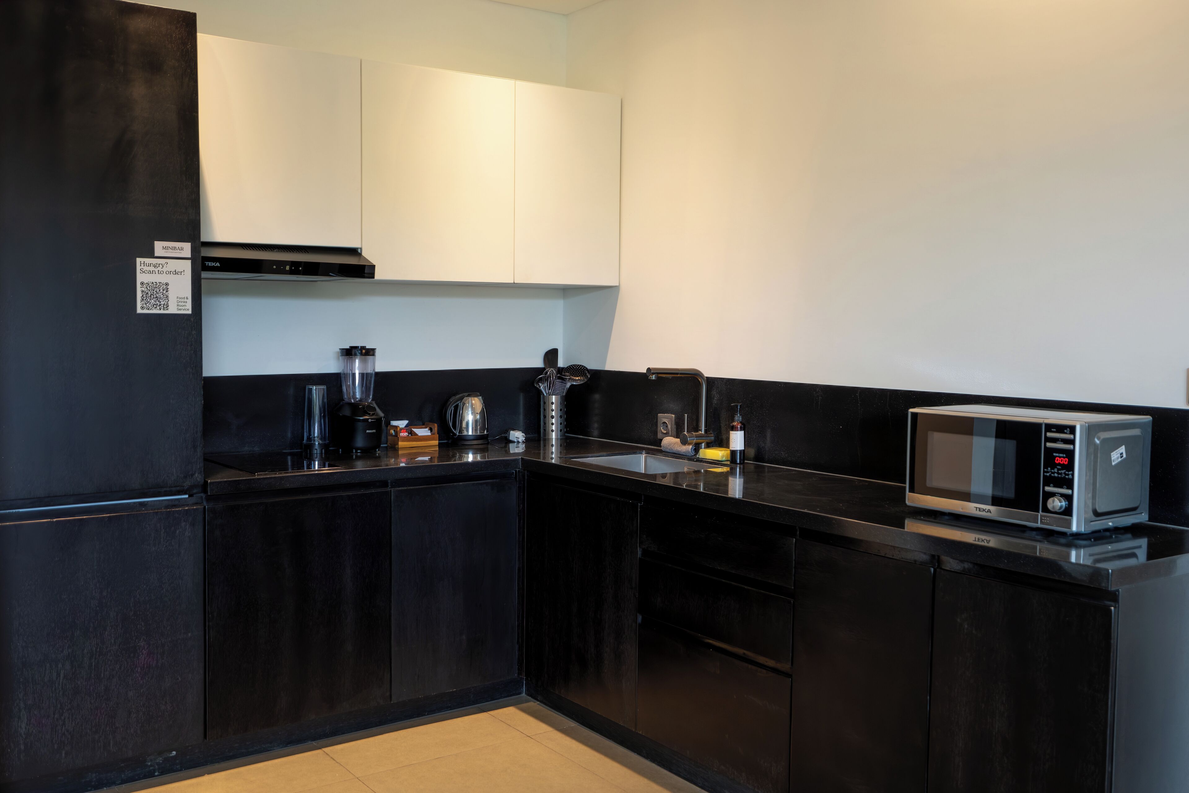 A modern kitchen with black cabinetry, a stainless steel microwave, and a coffee maker.