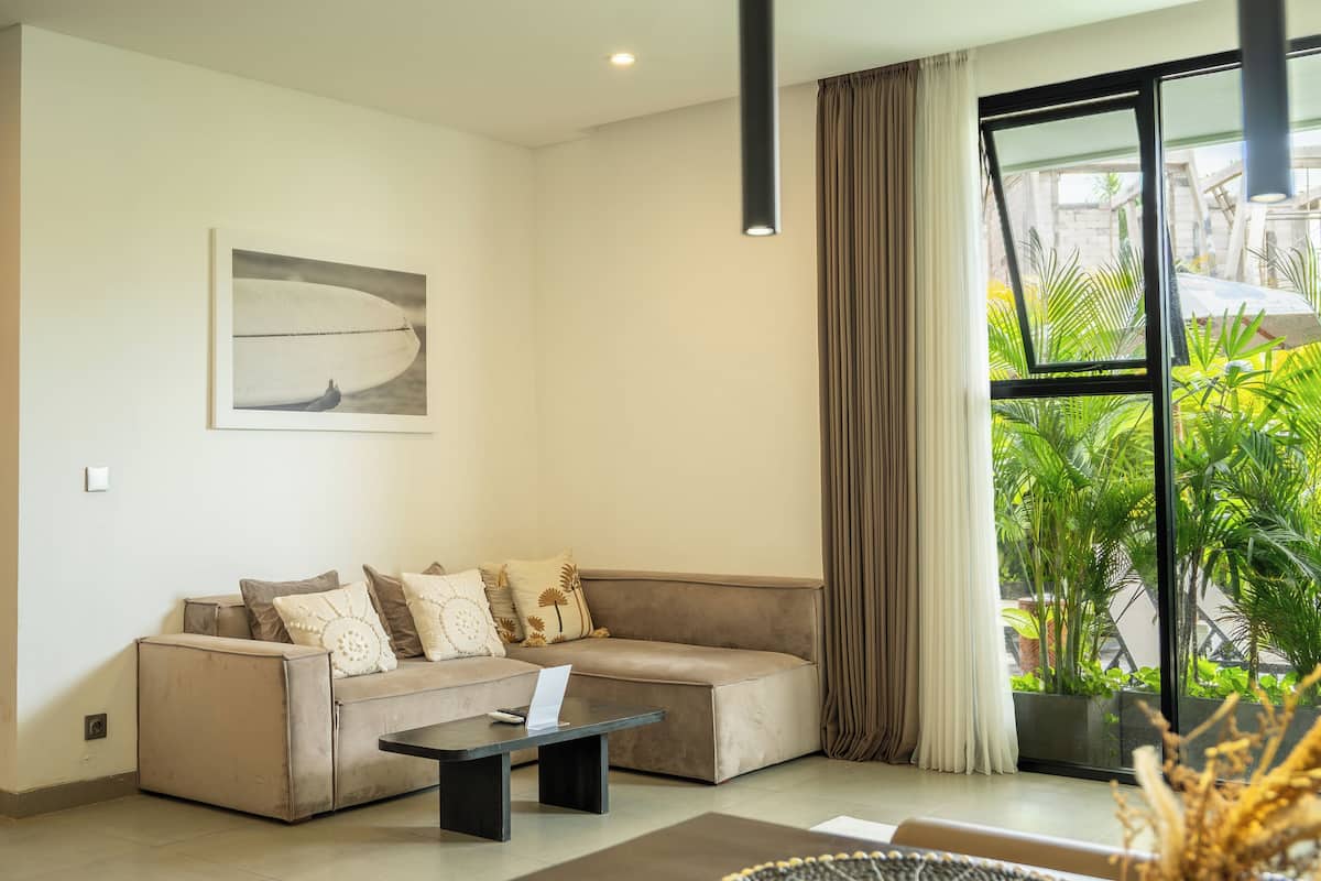A modern living room with a beige sofa, a coffee table, and a large window with curtains.