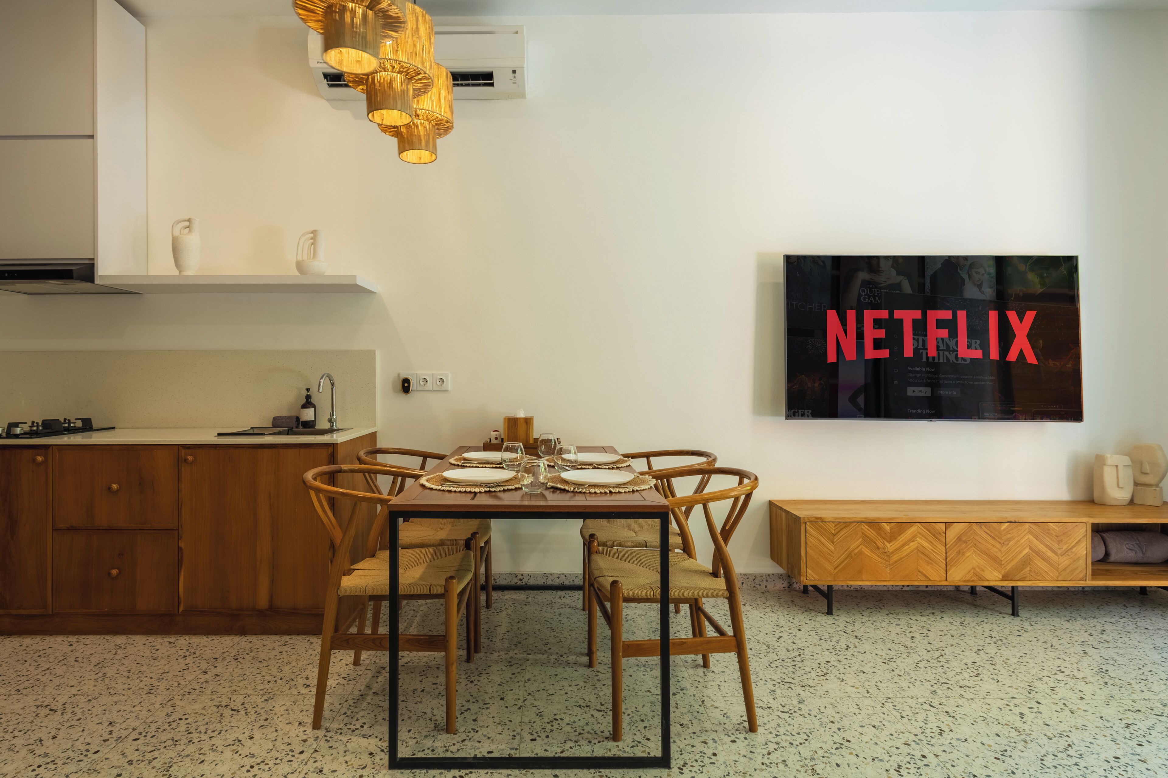 Una cocina moderna con una mesa de comedor para cuatro personas, un televisor montado en la pared y un armario de madera.