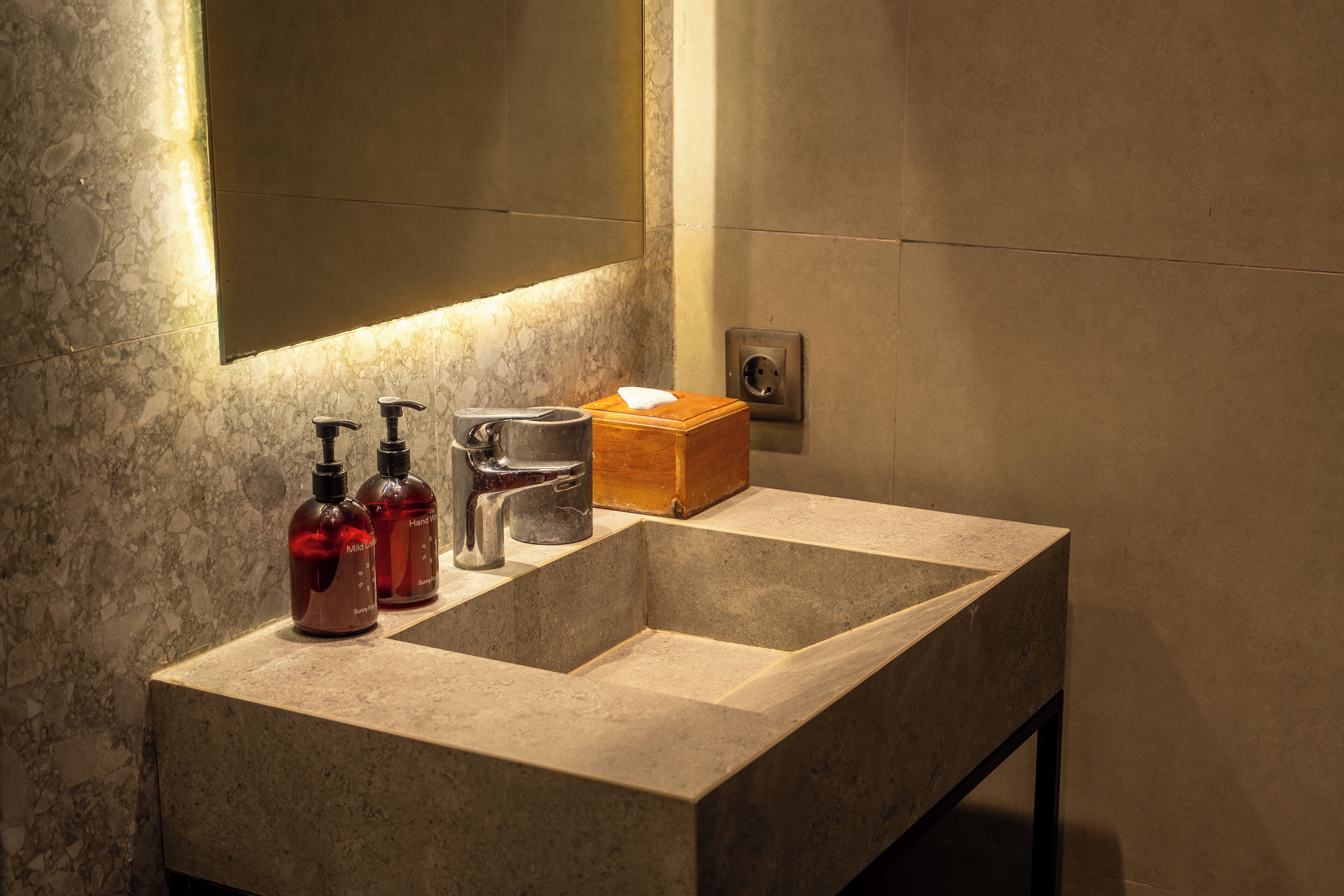 A bathroom with a marble sink, two hand soap bottles, a glass, and a tissue box.