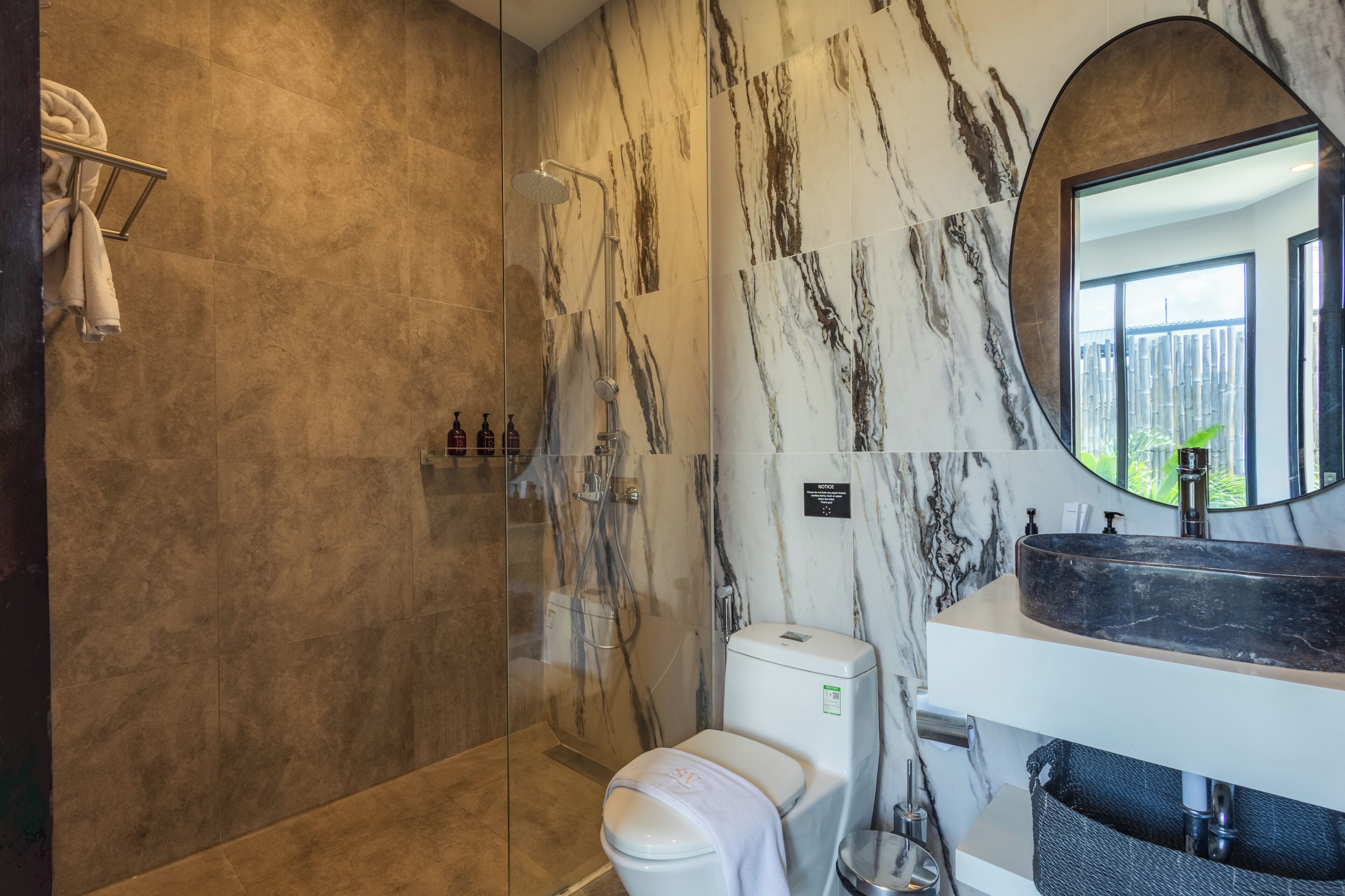 A bathroom with a glass-enclosed shower, a toilet, a sink with a marble countertop, and a large mirror.