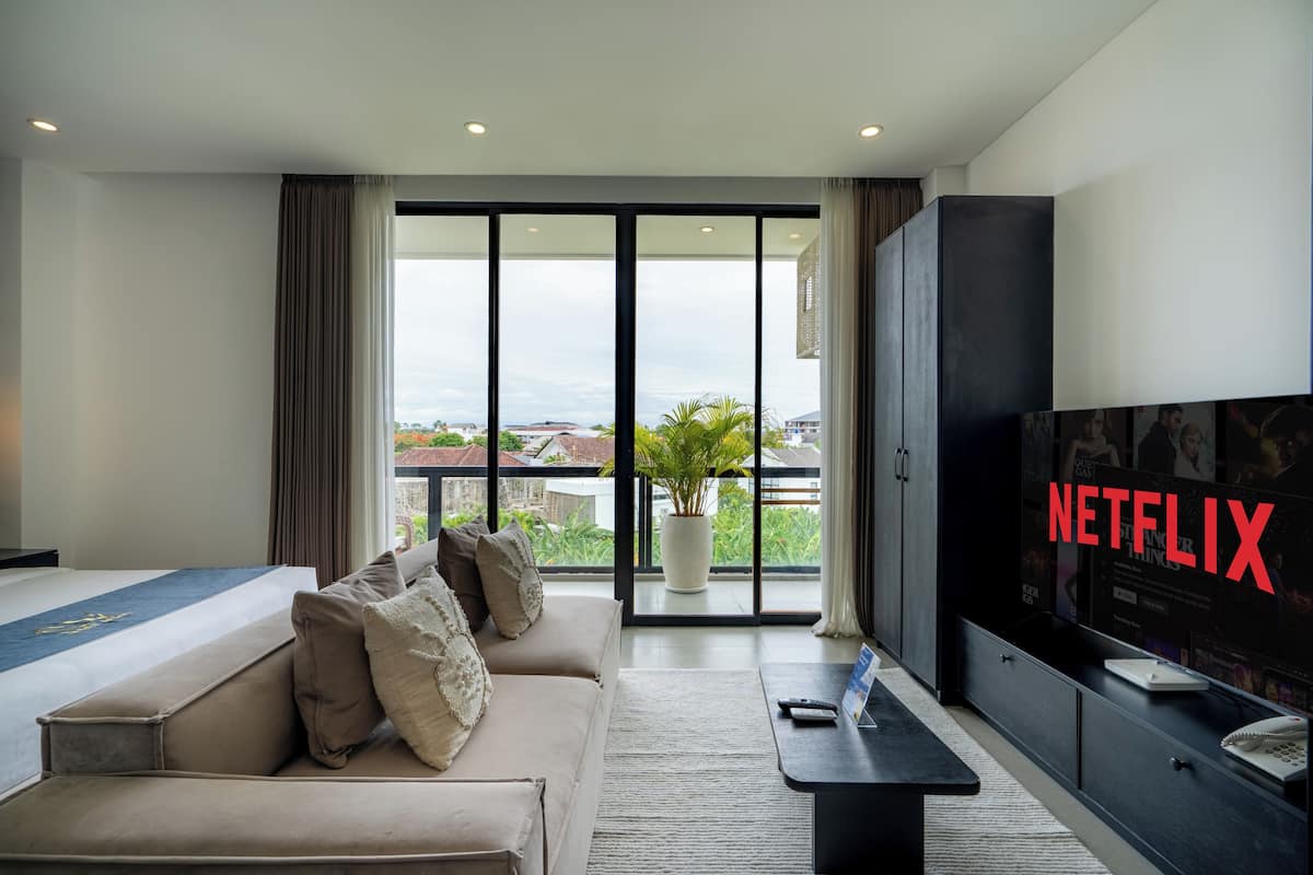 A modern hotel room with a large TV, a sofa, a coffee table, and a balcony with a view of the city.