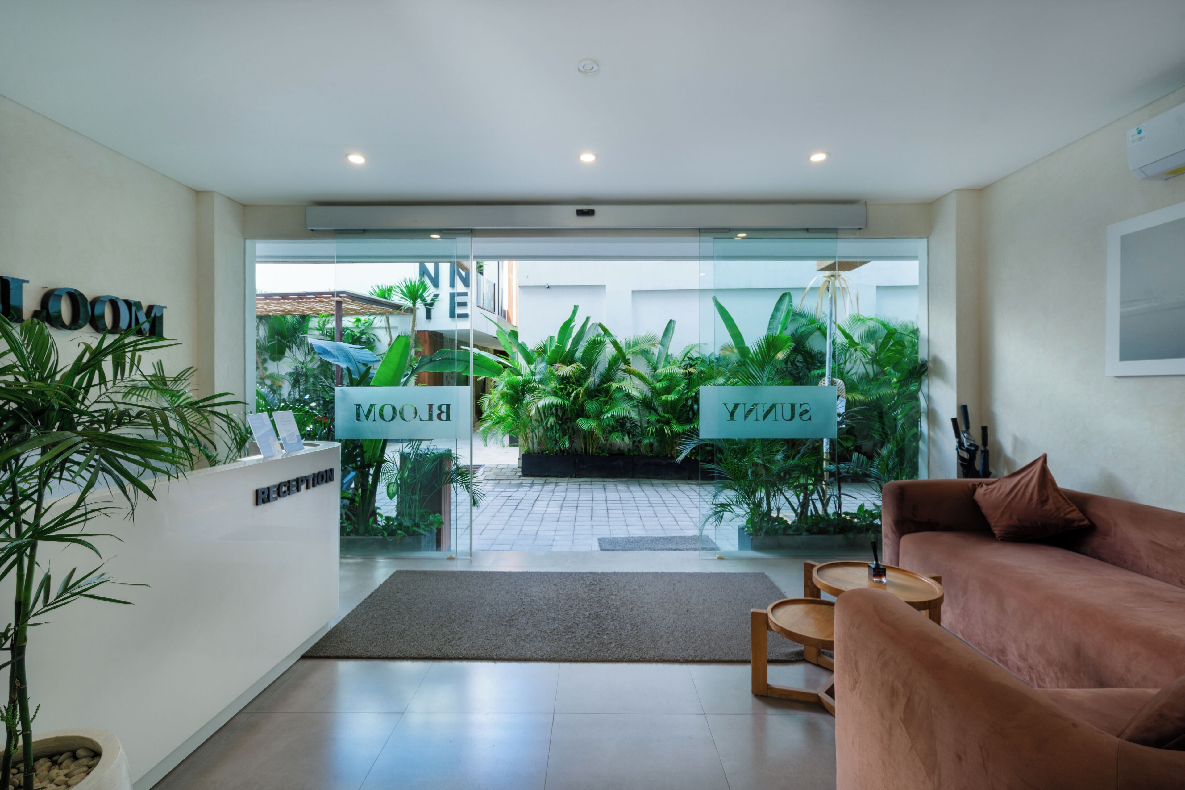 A reception area with a reception desk, a couch, and a glass door leading to a garden with plants.