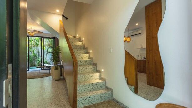 Ein modernes Interieur mit einer Wendeltreppe, einem großen Spiegel und Blick auf einen Balkon mit Pflanzen.