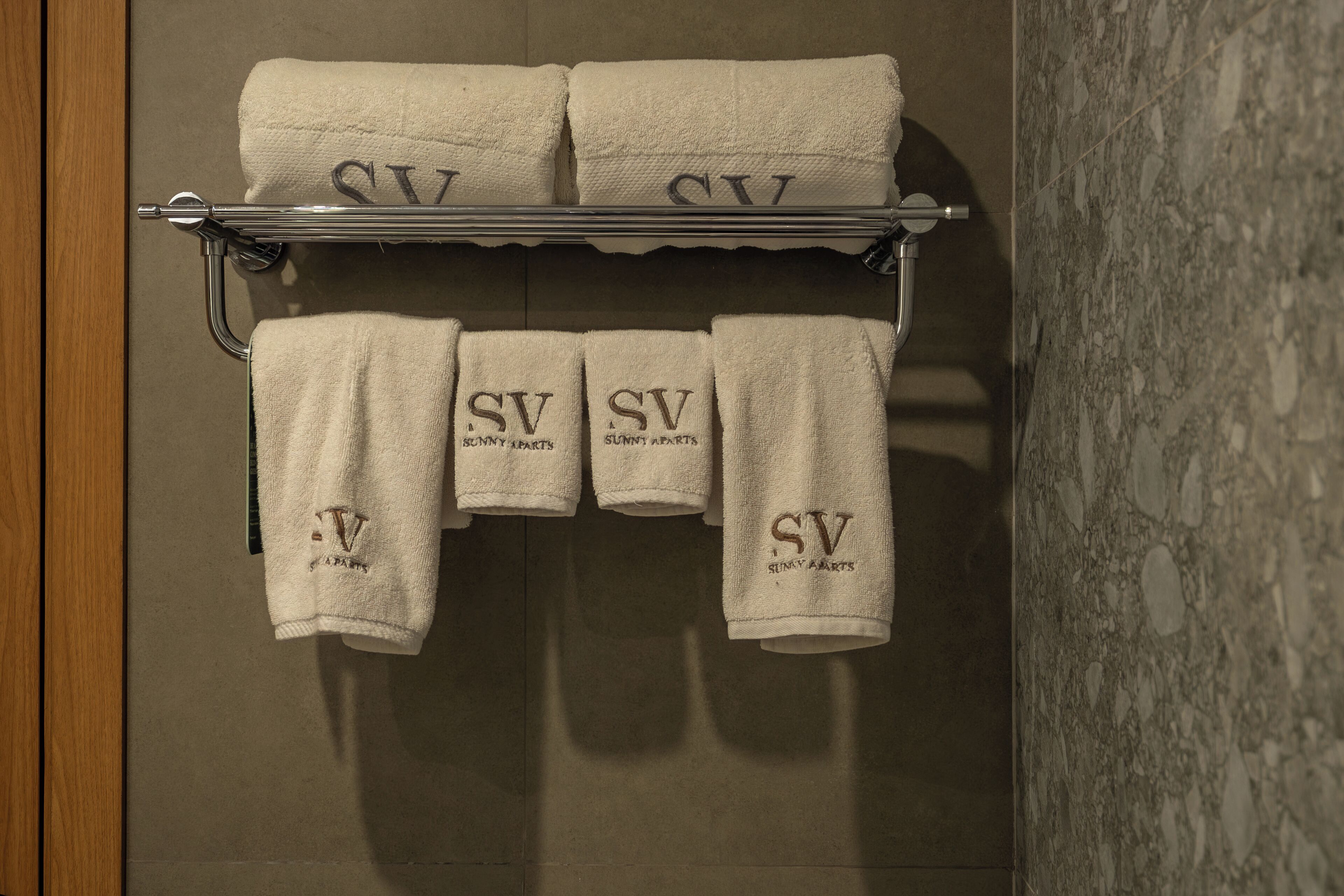 Un baño con un perchero que sostiene seis toallas, cada una con el bordado 'SV Sunny Apart'.