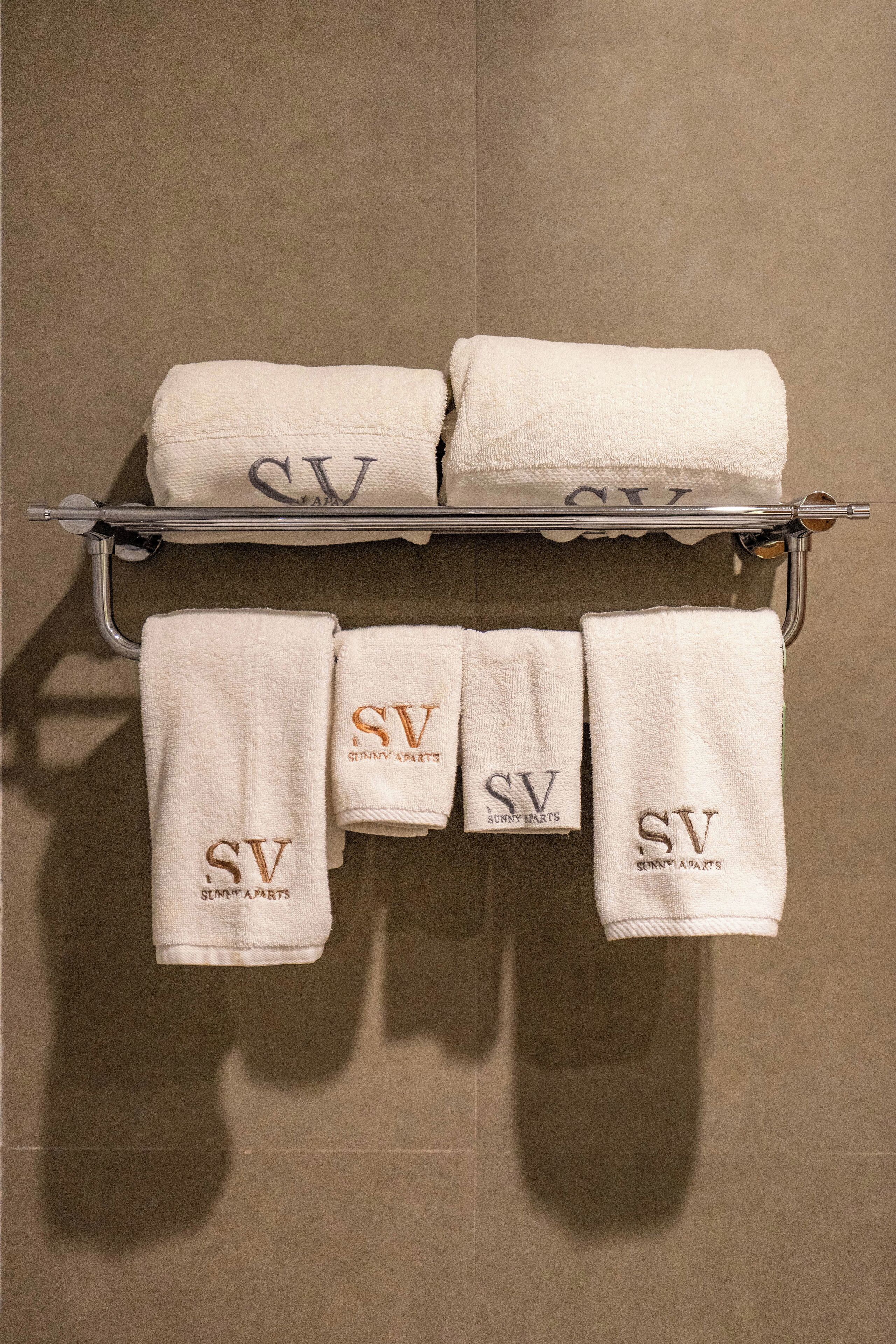 Un baño con un perchero que sostiene seis toallas blancas con el bordado "SV Sunny Parts".