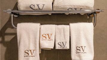Un baño con un perchero que sostiene seis toallas blancas con el bordado "SV Sunny Parts".