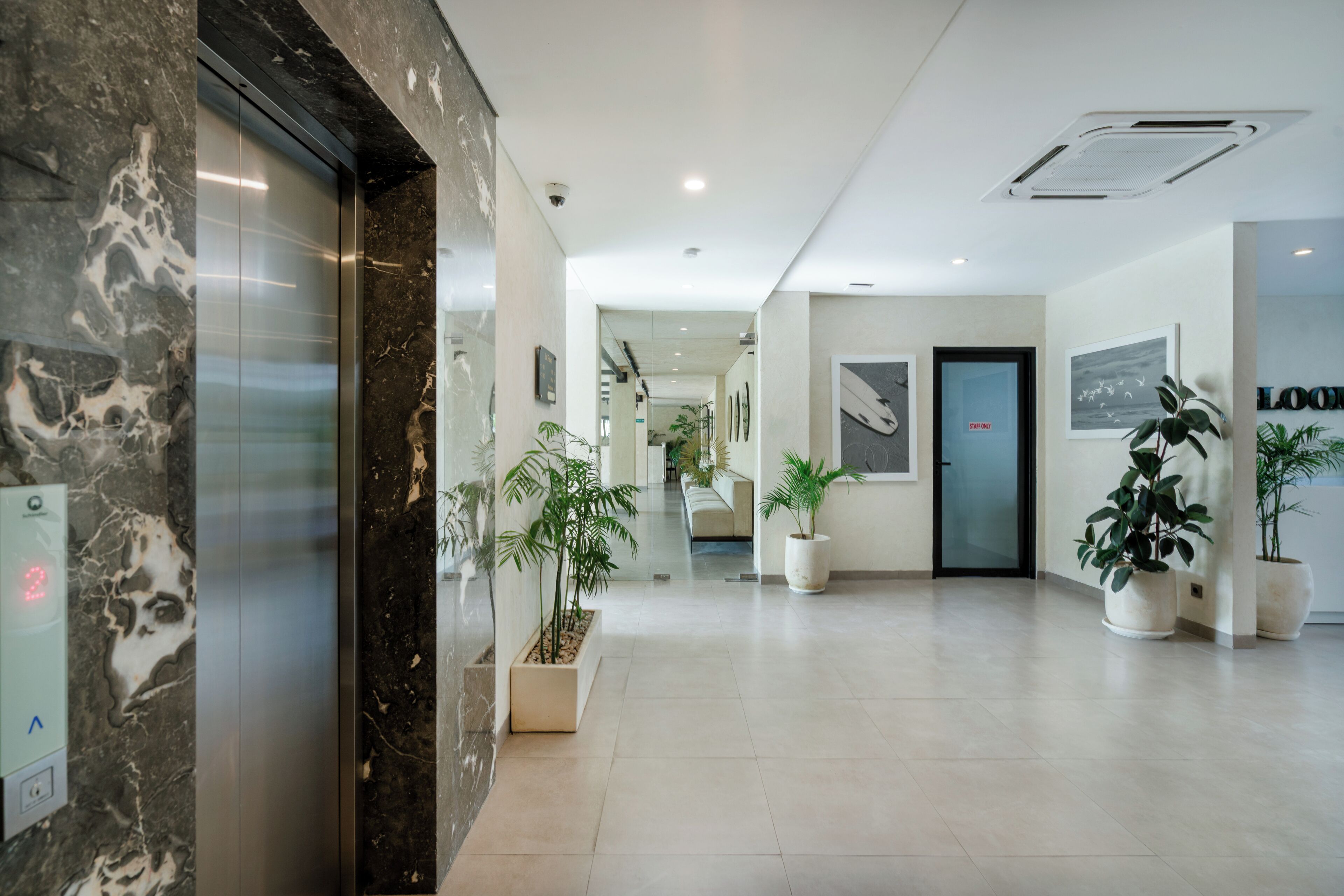 A modern hotel lobby with a marble reception desk, a reception area, and a 'Staff Only' door.