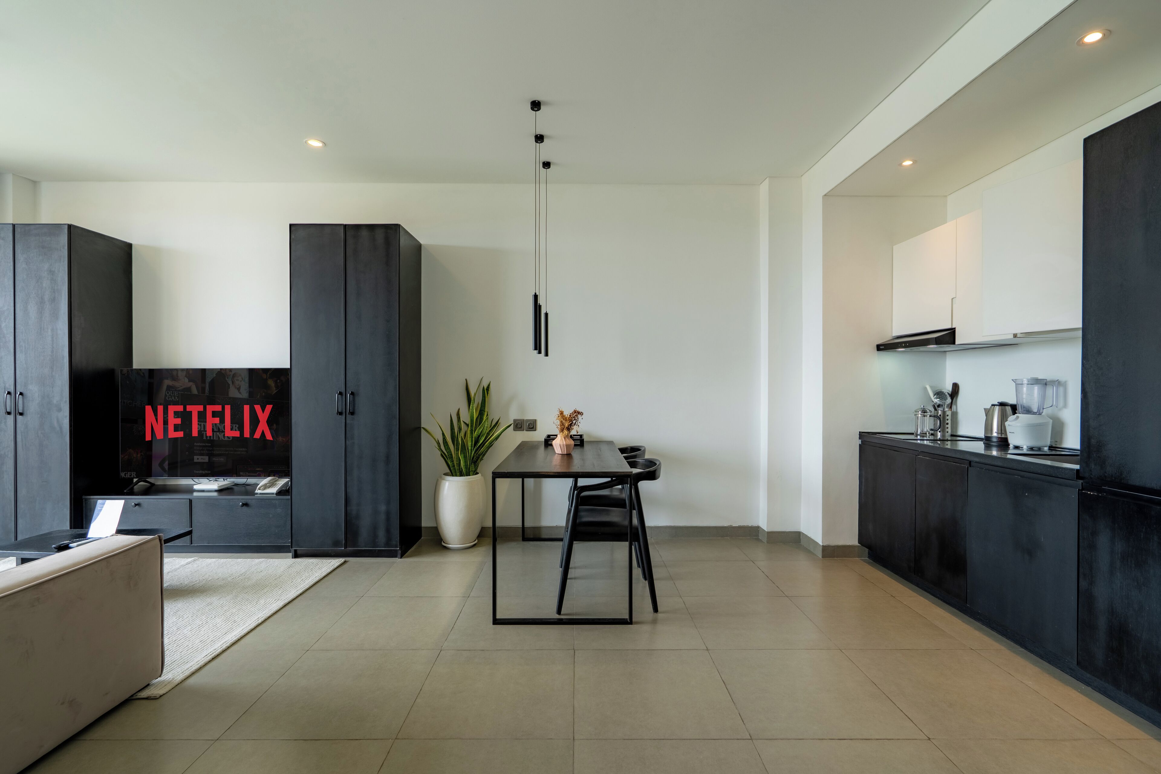 Une cuisine moderne avec des meubles de couleur sombre, un coin repas comprenant une table et des chaises, et une grande plante en pot.