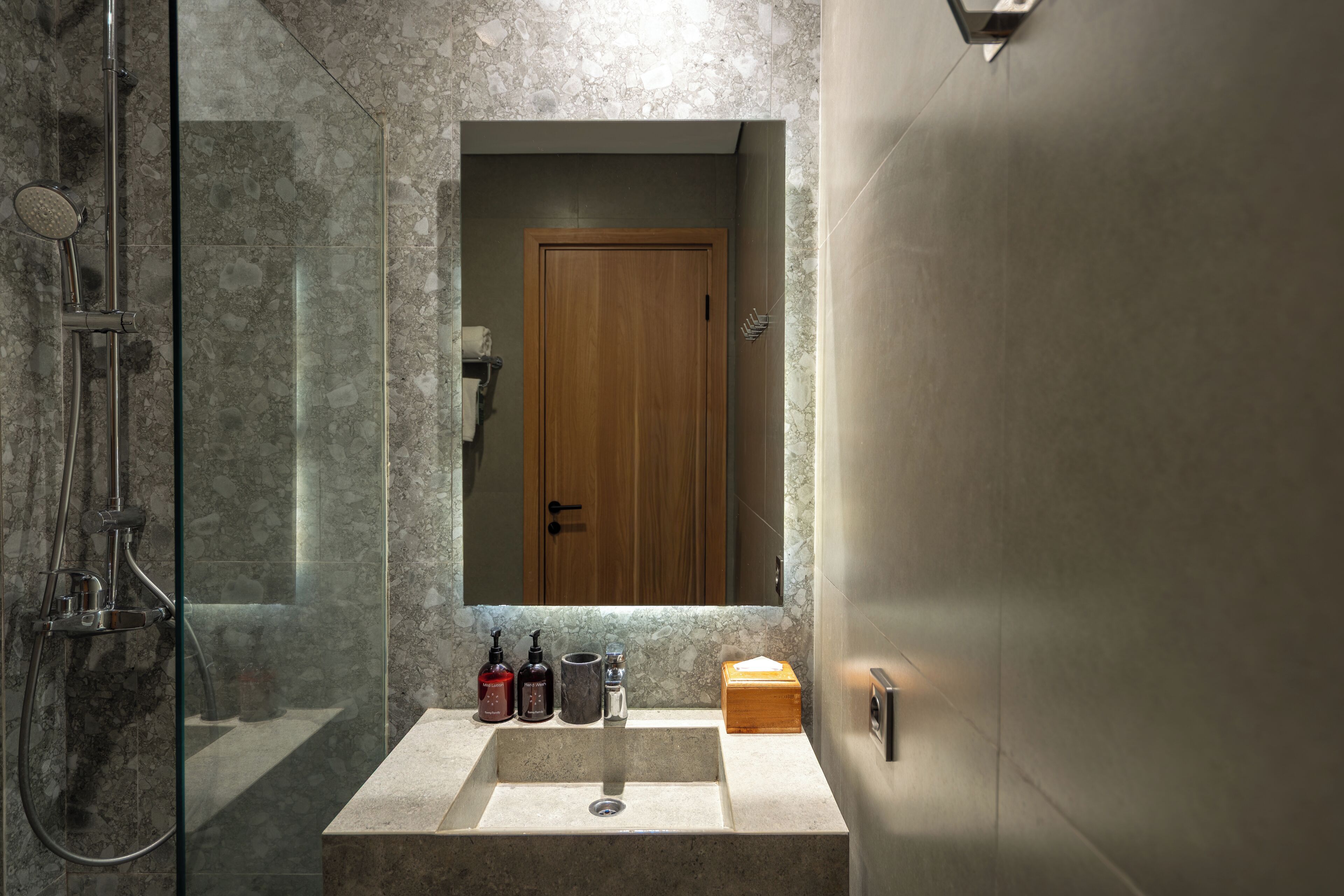 A bathroom with a glass-enclosed shower, a sink with a marble countertop, and a wooden door.