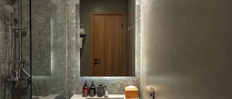A bathroom with a glass-enclosed shower, a sink with a marble countertop, and a wooden door.