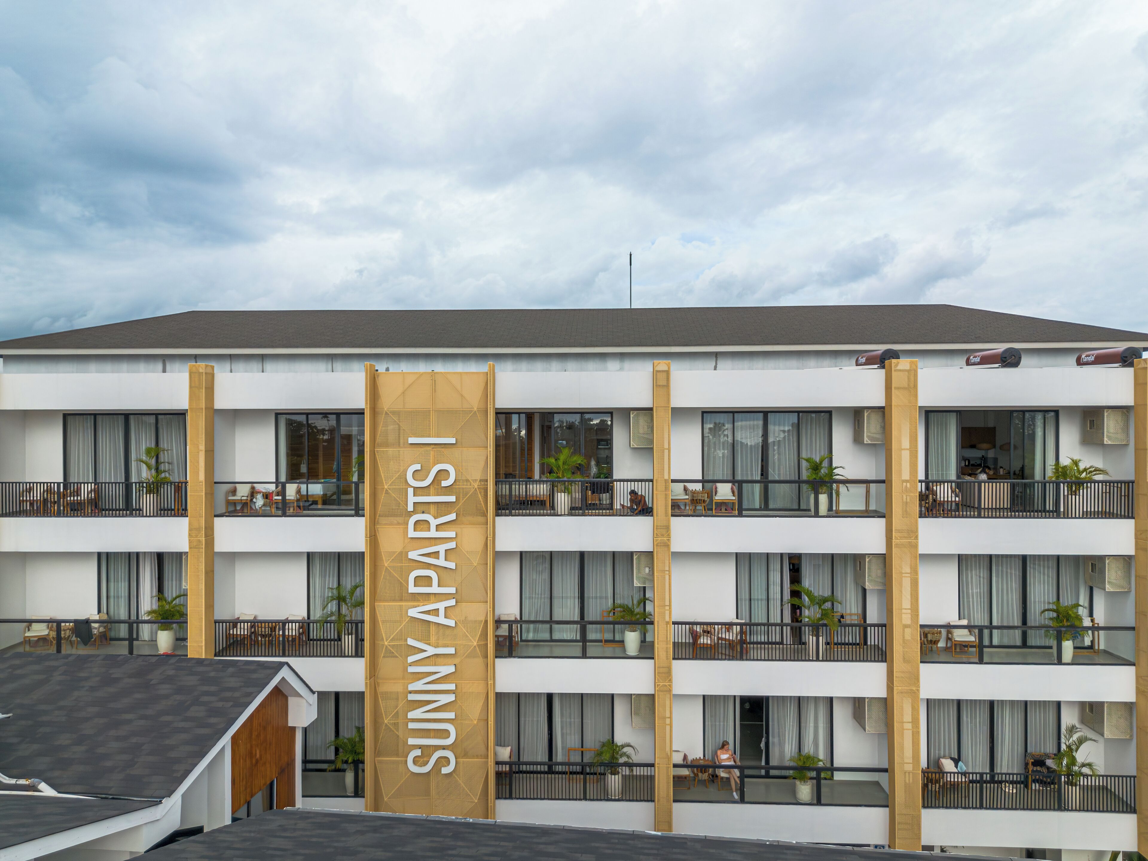 A multi-story hotel with a prominent 'Sunny Apart' sign, balconies with outdoor furniture, and large windows.