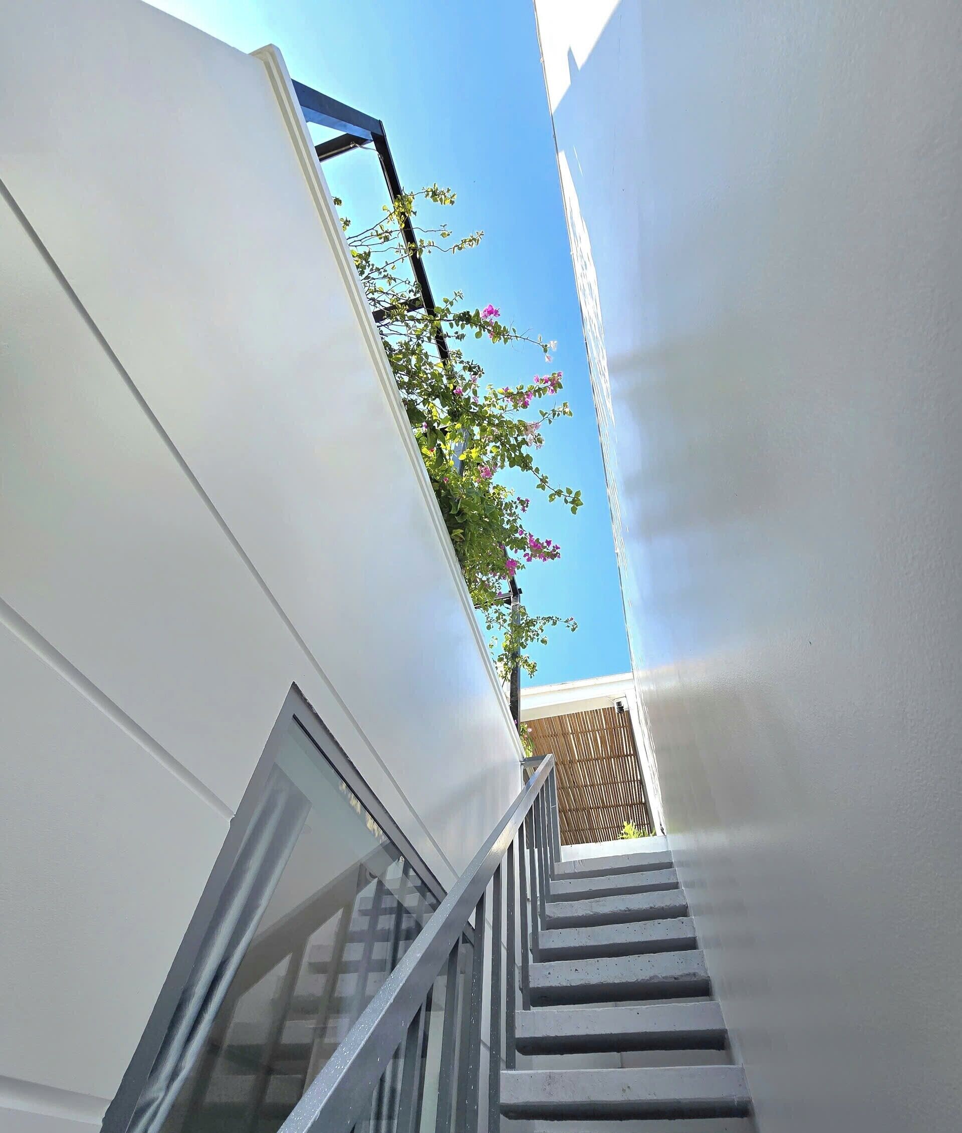 A modern staircase with a glass door leading to a balcony with a view of a clear sky and a wooden fence.