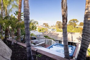 Un jacuzzi rodeado de palmeras, una terraza y vistas a casas vecinas.