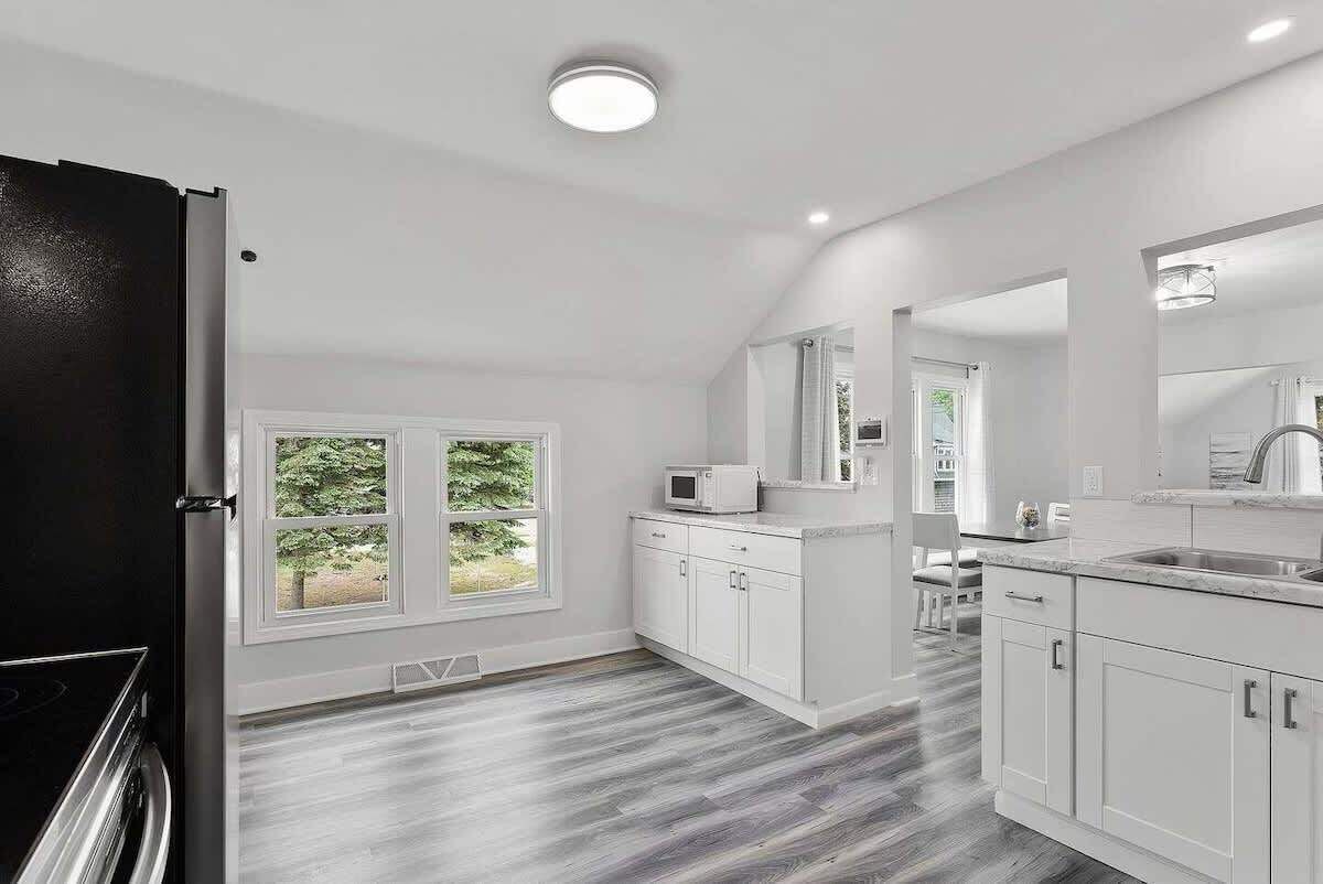 A modern kitchen with white cabinetry, a black refrigerator, and a window with a view of greenery.