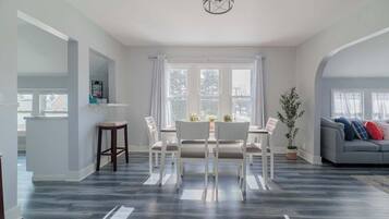 A spacious living area with a dining table and chairs, a gray sofa, and a large window with curtains.