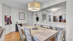 A modern kitchen with a dining area, a clock, and a framed menu on the wall. - Newly Renovated Beachfront Condo Pool & Balcony 108 Summerhouse by Avantstay (Isle of Palms)