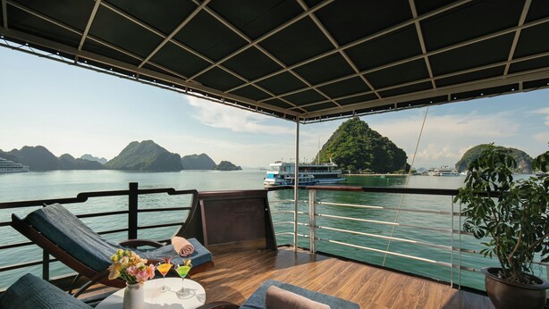 A deck with a view of the water, lounge chairs, a table with drinks, and a potted plant. - Mila Lux Cruise  (Tuan Chau)