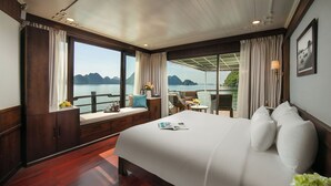 A bedroom with a large bed, a window with a view of the sea, a balcony with a table and chairs, and a wooden floor. - Mila Lux Cruise  (Tuan Chau)