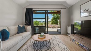 A modern living room with a sofa, coffee table, TV, and a sliding glass door leading to an outdoor area. - Studio on Martin Lane (Wānaka)
