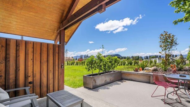 An outdoor patio with a wooden pergola, seating, and a view of a landscaped garden. - Studio on Martin Lane (Wānaka)