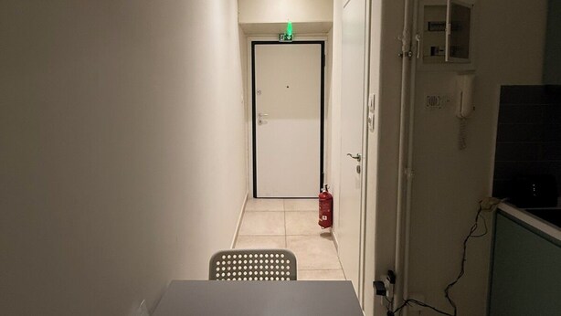 Ein schmaler Flur mit einem Tisch, Stühlen, einem Feuerlöscher und einer Tür am Ende.