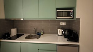 Eine kompakte Küche mit türkisfarbenen Schränken, einer Mikrowelle, einem Spülbecken und einer Kaffeemaschine.