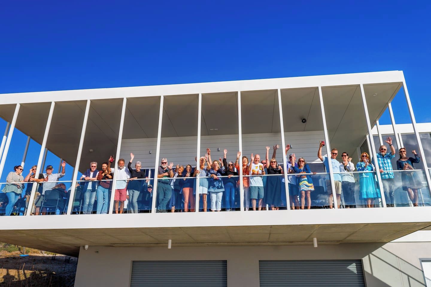 Un groupe de personnes se trouve sur un balcon, avec un ciel bleu dégagé au-dessus d’elles.