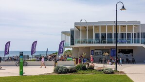 Um edifício moderno com fachada de vidro, área de estar externa e vista para o mar.